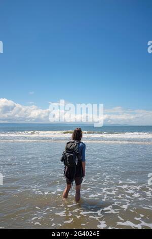 Frau, die in flachen Wellen an einem Sandstrand läuft. Stockfoto