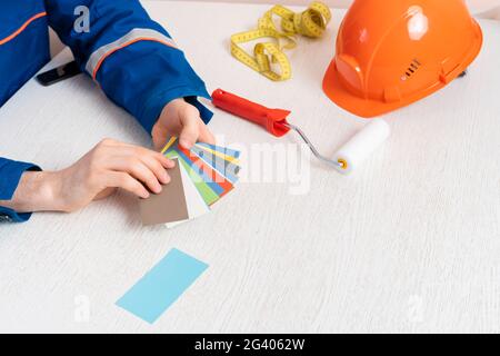 Männlicher Arbeiter, der Rollen- und Farbmusterproben hält, um die Wand im Raum zu lackieren Stockfoto