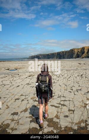 Frau, die am Nash Point, Wales, an einer felsigen Küste entlang geht. Stockfoto