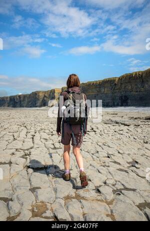 Frau, die am Nash Point, Wales, an einer felsigen Küste entlang geht.