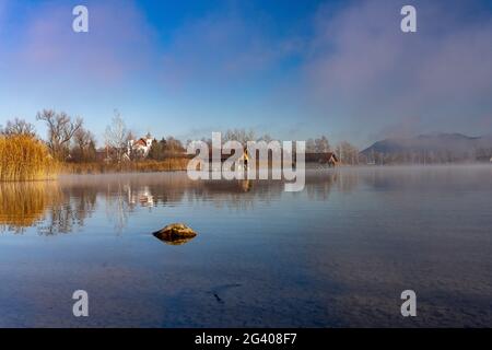 Bliock über die Kochelee nach Schlehdorf mit dem Kloster Schlehdorf und Fischerhütten am Ufer, Bayern, Deutschland. Stockfoto