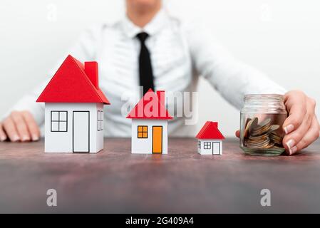 Sparen Sie für zu Hause. Geld sparen für Haus und Immobilien. Frau Hand Schutz auf Stapel Münzen und Hausmodell auf dem Tisch. Stockfoto