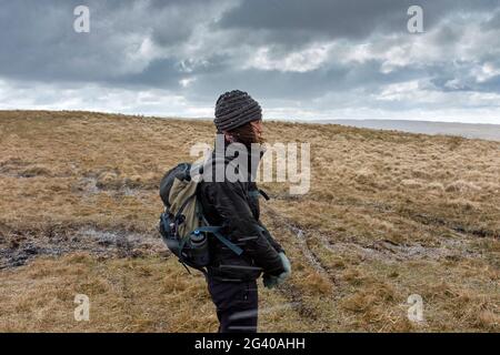 Frau, die bei einem Hagelsturm in Wales auf dem Hügel herumläuft. Stockfoto