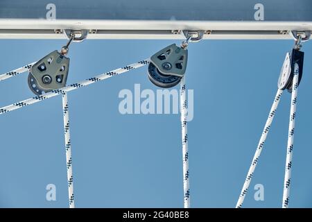 Nahaufnahme der Segelbootseile bei sonnigem Wetter, Seilrollen und Seile am Mast, Yachtsport, Schiffsausrüstung, Meer auf dem Rücken Stockfoto