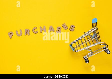Mini-Einkaufswagen auf gelbem Hintergrund mit dem Wort Käufe. Draufsicht Stockfoto