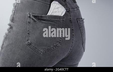 Menstruationspad in der Gesäßtasche der Damenjeans auf grauem Hintergrund Stockfoto