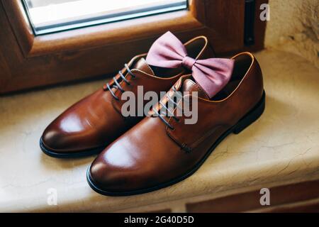 Stylische Fliege für den Bräutigam an Herrenschuhen aus braunem Echtleder auf der Fensterbank. Stockfoto