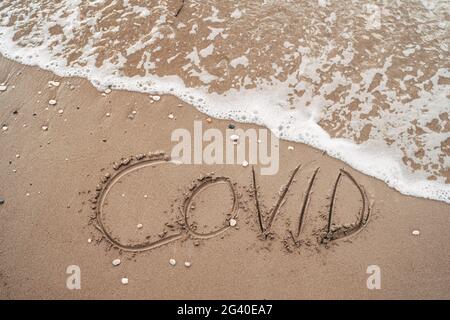 COVID Inschrift auf dem Sand in der Nähe des Meeres. Das Konzept der Annullierung von Reisen in den Jahren 2020 und 2021 aufgrund der Coronavirus-Pandemie in Stockfoto