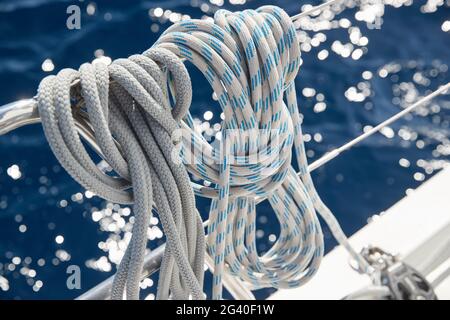 Nahaufnahme der Segelbootseile bei sonnigem Wetter, Seilrollen und Seile am Mast, Yachtsport, Schiffsausrüstung, Meer auf dem Rücken Stockfoto