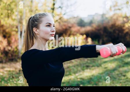 Fröhliche Fitness-Frau beim Training mit Hanteln vor der Tür. Mädchen Heben freie Gewichte im Sommer. Stockfoto