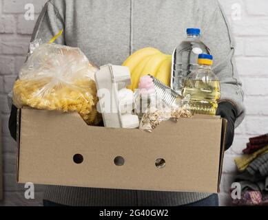 Frau in einem grauen Pullover verpackt Lebensmittel in einen Karton, das Konzept der Hilfe und Freiwilligenarbeit Stockfoto