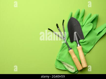 Grüne Gummihandschuhe und Garten-Set aus Schaufeln, Rechen, Mistgabeln auf grünem Hintergrund Stockfoto