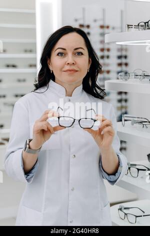 Ein hübscher Augenarzt hält eine Brille für einen Versuch. Optiker bietet an, eine Brille zu tragen. Stockfoto