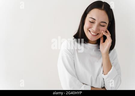 Nettes, schüchternes Mädchen, das auf einem weißen Hintergrund schön lächelt. Mädchen auf einem Hintergrund von leerer Wand, kopieren Raum, Ort für Text. Stockfoto