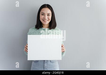 Die junge hübsche Frau lächelt und hält ein leeres Stück Papier in den Händen. Modell. Kopieren Sie Platz für Ihren Text. Stockfoto