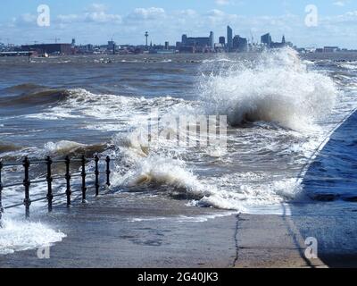 Krachende Wellen auf der Promenade in New Brighton mit Liverpool Waterfront im Hintergrund Stockfoto