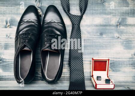 Schwarze Leder Herrenschuhe mit Manschettenknöpfen in einer rot-weißen Box mit einer gepunkteten Krawatte auf einer Holzstruktur. Stockfoto