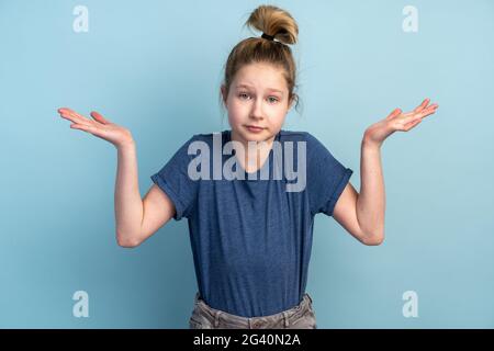 Verwirrendes Teenager-Mädchen auf blauem Hintergrund spreizt seine Arme. Das Mädchen sticht, zeigt, dass sie nichts weiß. Stockfoto