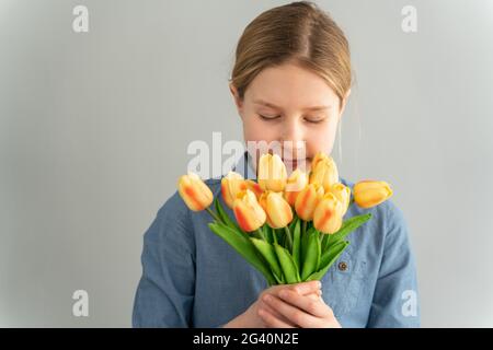 Nettes Mädchen mit einem Strauß gelber Tulpen auf weißem Hintergrund. Das Teenager-Mädchen schnüffelt wunderschöne Blumen, schloss die Augen auf einem weißen Hintergrund. Stockfoto