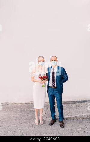 Braut und Bräutigam in medizinischen Masken auf grauem Hintergrund. Hochzeit für zwei während der Isolation, Covid-19 Pandemie. Banner mit Copyspa Stockfoto