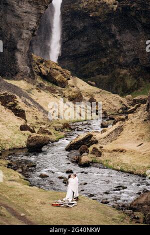 Reiseziel Island Hochzeit, in der Nähe des Kvernufoss Wasserfalls. Ein Brautpaar steht unter einem karierten Dach in der Nähe eines Bergflusses. Der Bräutigam h Stockfoto