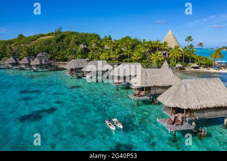 Luftaufnahme, wie das Frühstück vom Pirogue-Outrigger-Kanu zu einem Überwasser-Bungalow des Sofitel Bora Bora Private Island Resort in Bora gebracht wird Stockfoto