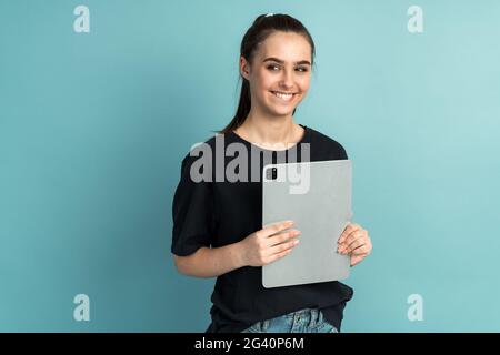 Foto von fröhlichen niedlichen netten charmanten Mädchen hält Tablet mit ihren Händen. Lächelnd zahnhaft isoliert auf blauem Hintergrund, Foto von fröhlich niedlich schön c Stockfoto