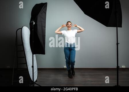 Mädchen macht Gesten des Sieges und des Friedens, posiert sie in einem Fotostudio. Der Prozess der Aufnahme in einem Fotostudio. Stockfoto