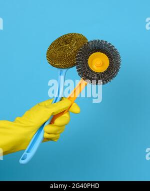 Hand in einem gelben Handschuh hält einen Stapel Plastikbürsten, blauer Hintergrund Stockfoto