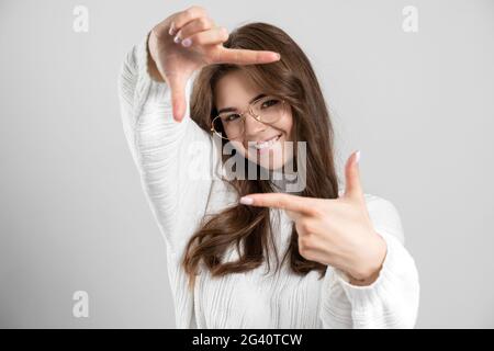 Portrait der positiven fröhlichen Mädchen macht Daumen nach oben Zeichen, sie macht Foto. Mädchen trägt einen schönen Pullover isoliert auf einem grauen Hintergrund., Stockfoto
