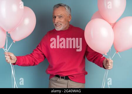 Foto eines attraktiven, älteren Mannes mit rosa Luftballons. Isoliert auf rosa Hintergrund., Foto von einem attraktiven, älteren Mann hält rosa Ballons. Isol Stockfoto