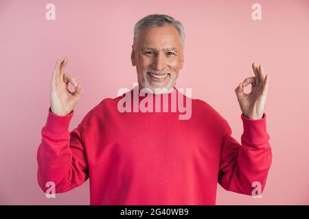 Lächelnder Mann meditiert auf einem rosa Hintergrund. Das Konzept der Spiritualität, des Glaubens. Stockfoto