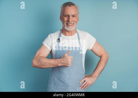 Ein fröhlicher, positiver Rentner zeigt Daumen nach oben, trägt eine Schürze. Mann isoliert auf Kopierplatz, für Text platzieren Stockfoto