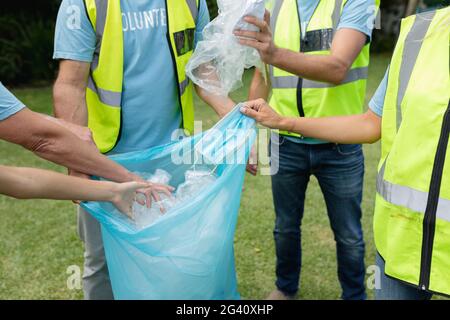 Mittelteil der kaukasischen Multi-Generation-Gruppe sammeln Plastikmüll und Gesichtsmaske im Feld Stockfoto