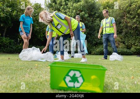 Kaukasische Gruppe von Männern und Frauen sammeln Müll auf dem Feld Mit Recycling-Box im Vordergrund Stockfoto