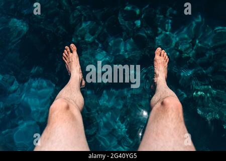 Der Mensch senkte seine Füße ins blaue Meer. Aktive Erholung am Meer Stockfoto