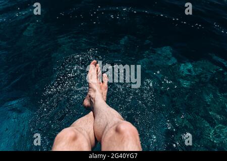 Gekreuzte, männliche Beine in das blaue Wasser abgesenkt. Entspannter Mann am Meer Stockfoto