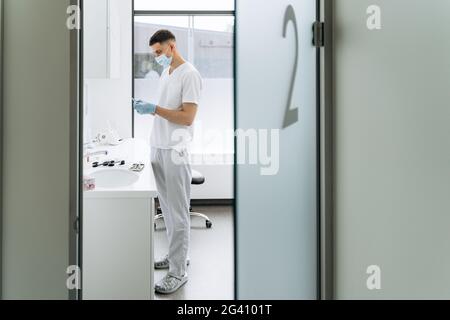 Im Büro arbeitet ein ernsthafter, junger Zahnarzt. Der Arzt bereitet die Werkzeuge für die Arbeit vor Stockfoto