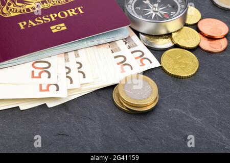 Eine Anordnung von Euro-Scheinen, Münzen, Reisepass und Kompass auf Schiefer. Stockfoto