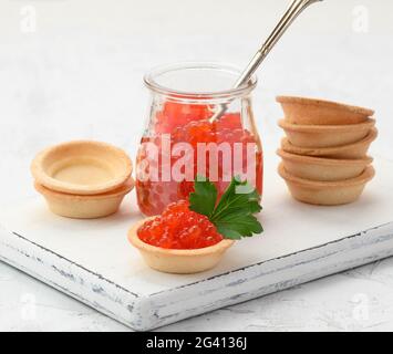 Roter Kaviar im Glasgefäß und runde Törtchen auf einem weißen Tisch Stockfoto