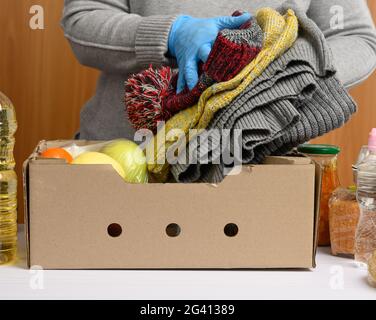 Frau in Handschuhen sammelt immer wieder Lebensmittel, Früchte und Dinge und einen Karton, um Bedürftigen zu helfen Stockfoto