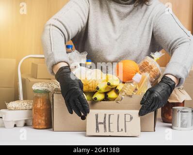 Frau in einem grauen Pullover verpackt Lebensmittel in einen Karton, das Konzept der Hilfe und Freiwilligenarbeit Stockfoto