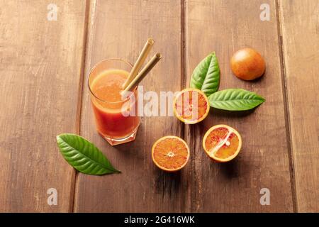 Ein Glas frischen Orangensaft mit Blutorangen, grünen Blättern und zwei Bambusstrohhalmen Stockfoto