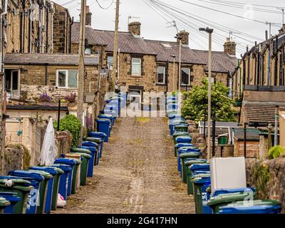 Schräge gepflasterte Hintergasse hinter viktorianischen Reihenhäusern in Skipton, Großbritannien, mit Reihen von Mülltonnen. Stockfoto