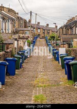 Schräge gepflasterte Hintergasse hinter viktorianischen Reihenhäusern in Skipton, Großbritannien, mit Reihen von Mülltonnen. Stockfoto