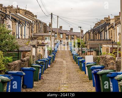 Schräge gepflasterte Hintergasse hinter viktorianischen Reihenhäusern in Skipton, Großbritannien, mit Reihen von Mülltonnen. Stockfoto