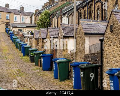 Schräge gepflasterte Gasse hinter viktorianischen Reihenhäusern in Skipton, Großbritannien, mit Reihen von Mülltonnen. Stockfoto