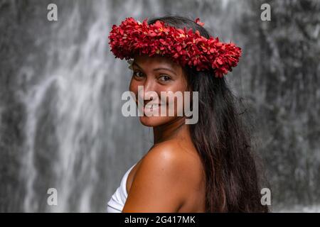 Porträt einer hübschen jungen Tahitianerin mit Blumenkopf vor einem Wasserfall in den Wassergärten von Vaipahi, Teva i Uta, Tahiti, Windward Stockfoto