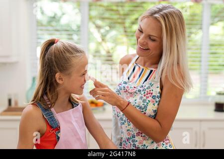 Lächelnde kaukasische Mutter und Tochter tragen Schürzen und haben Spaß beim Backen Zusammen in der Küche Stockfoto