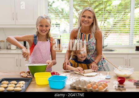 Lächelnde kaukasische Mutter, Tochter und Sohn tragen Schürzen und backen gemeinsam in der Küche Kekse Stockfoto